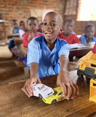 Picture of a child in class playing with two toy trucks.