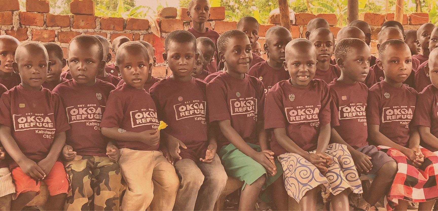 Picture of children in an Ugandan school smiling and sitting on a bench together in their school uniforms.